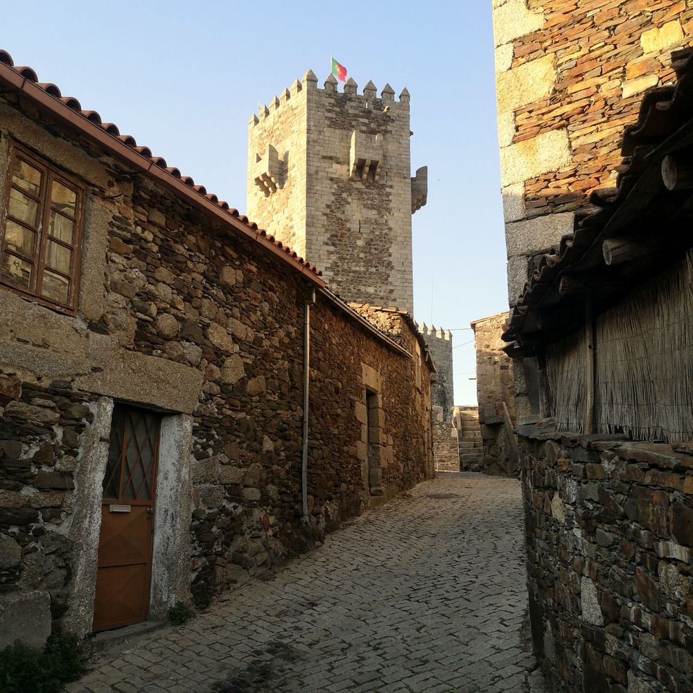 Torre almenada con bandera portuguesa al final de un callejón de piedra